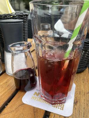 Ein Holztisch. darauf ein Glas mit Eiswürfel und Tee, daneben eine kleine Glaskaraffe mit roten Johannisbeerensirup
