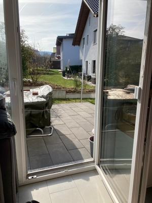 Eine offene Terassentür mit Blick auf den sonnenbeschienen Garten mit blauem Himmel